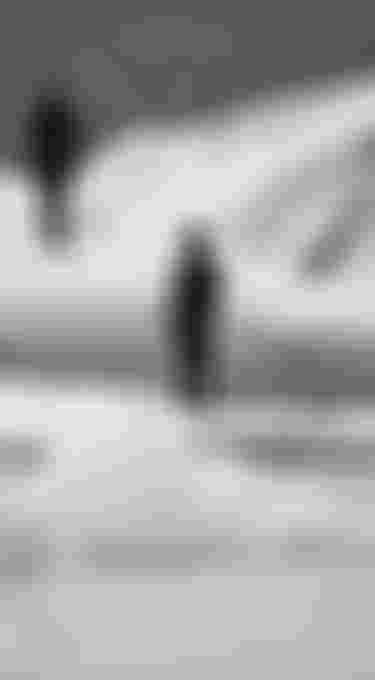 Two persons wearing black wetsuits with hood standing on floating ice