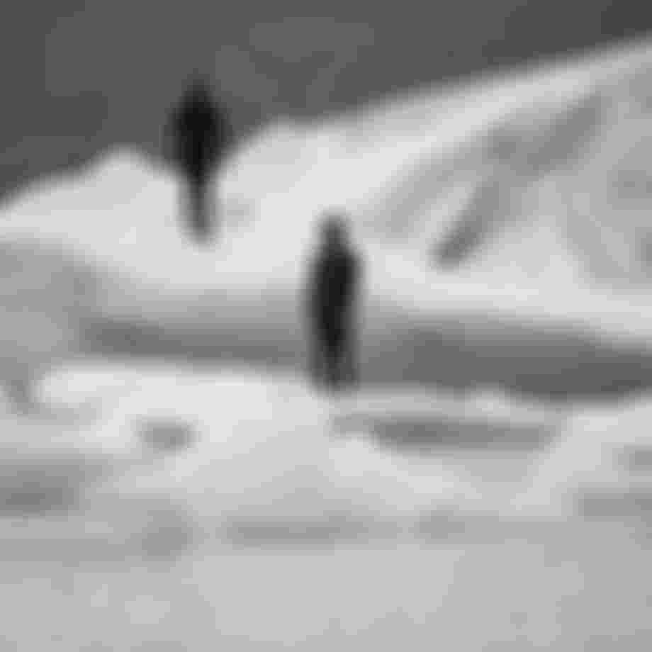 Two persons wearing black wetsuits with hood standing on floating ice