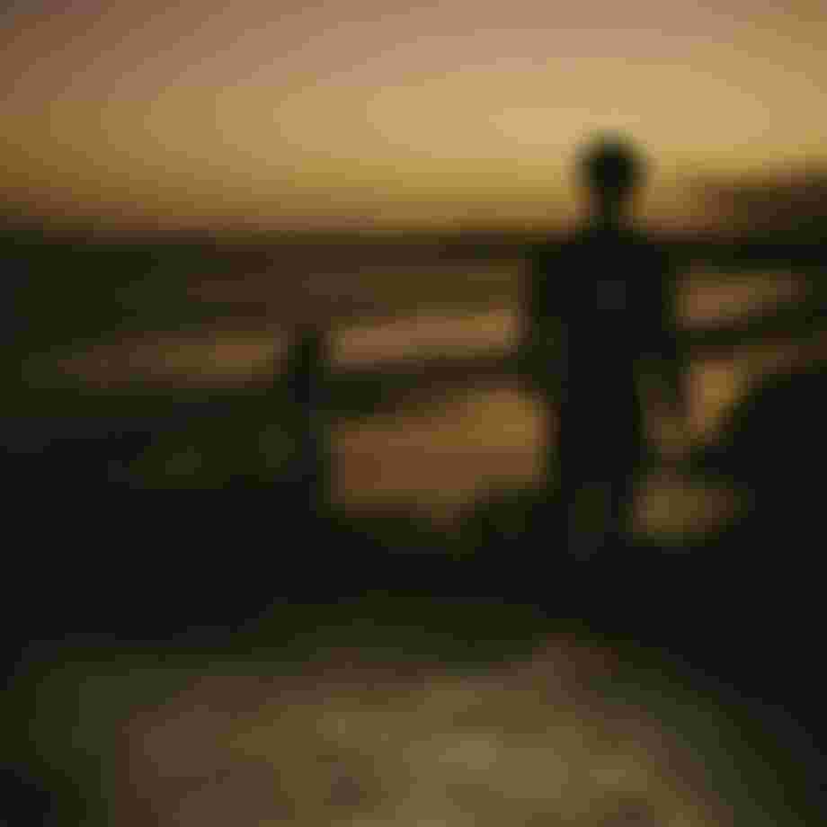 analog image of two people wearing wetsuits overlooking a beach at sunset