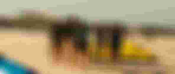 Group of women wearing black wetsuits standing in a circle at the beach with kites around them