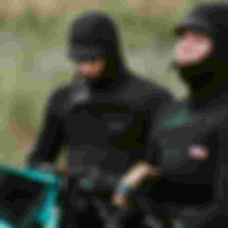 Two people with hooded wetsuits and kite equipment