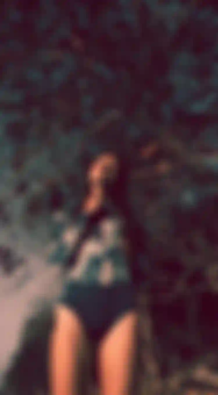 woman in a blue long sleeve swimsuit in front of trees with an analog grainy filter