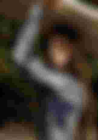 Woman in a blue patterned long sleeve swimsuit carrying a surfboard on her head