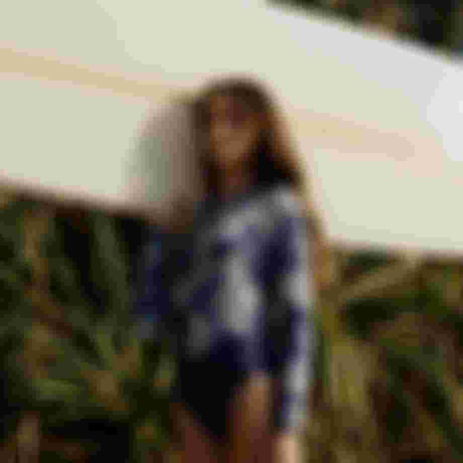 Woman in a blue longsleeve swimsuit carrying a longboard on her shoulder