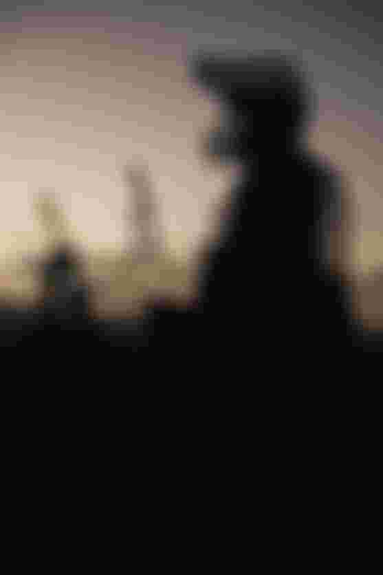 Silhouettes of people with bicycles stand against a dramatic sunset sky, creating a layered, reflective effect.