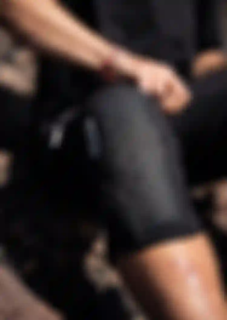 Person wearing a patterned knee pad, with visible leg scars, sitting outdoors on rocky terrain.