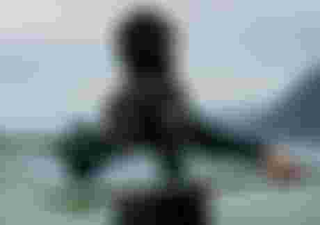 Woman in a hooded wetsuits carrying a kite surfboard on a misty beach