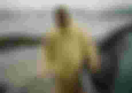 Man in yellow rain coat standing on a misty beach and holding a kite in his hand