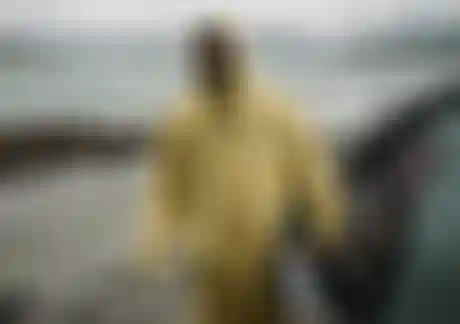 Man in yellow rain coat standing on a misty beach and holding a kite in his hand