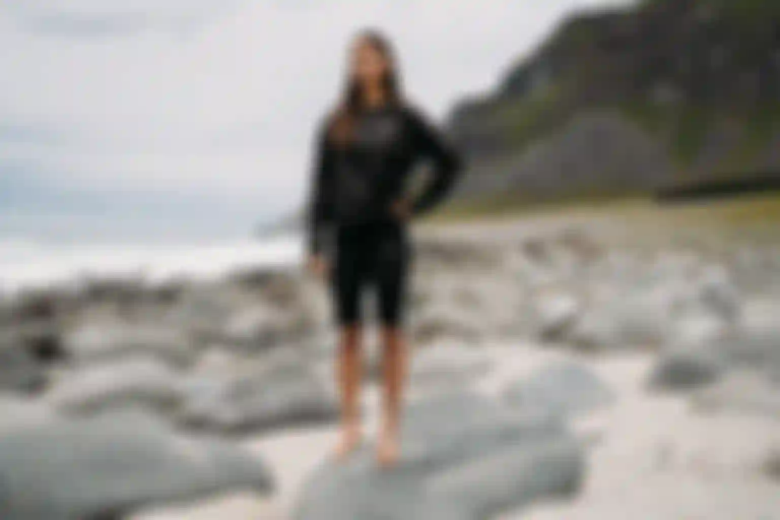 Woman in black rashguard and short tights standing on a rocky beach