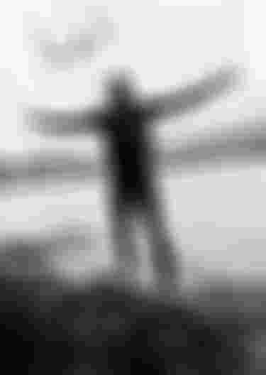 Kiteboarder standing on a grassy shore with arms stretched wide
