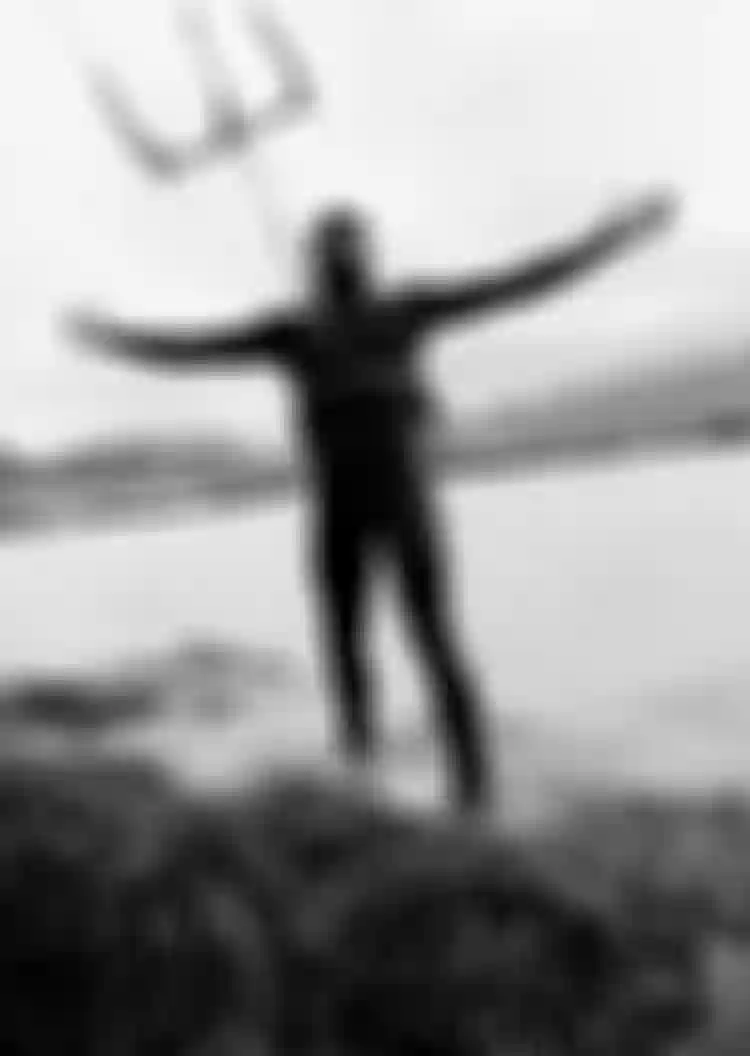 Kiteboarder standing on a grassy shore with arms stretched wide