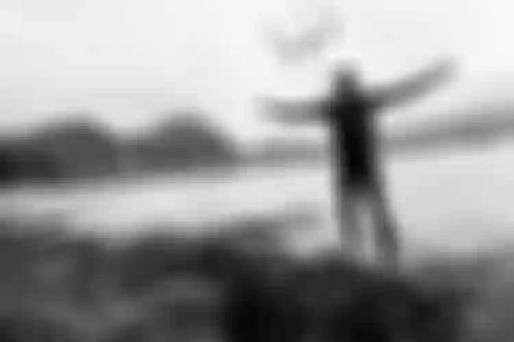 Kiteboarder standing on a grassy shore with arms stretched wide