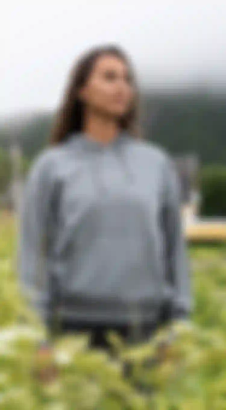 Woman wearing a grey sweater with ION logo standing in a grass field with a cloudy sky above