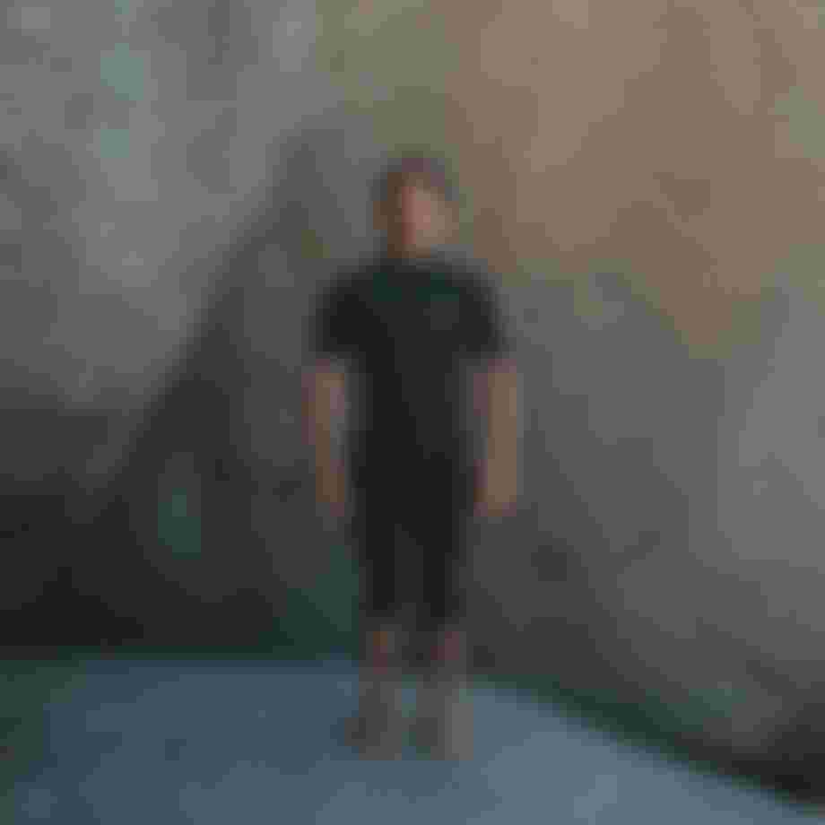 Man standing in front of big rocks wearing a black overknee shorty wetsuit with short sleeves