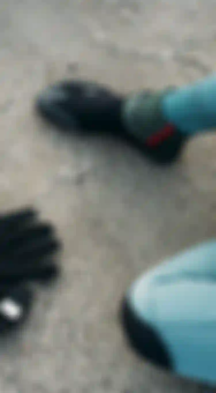 Woman in a green wetsuits sitting on the sand and putting on neo booties