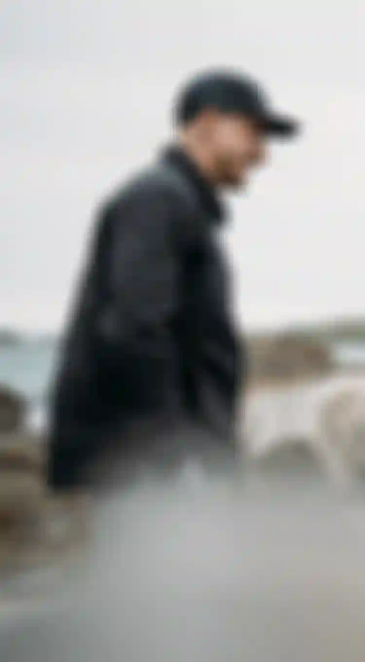 Two man in black jackets filming on the beach