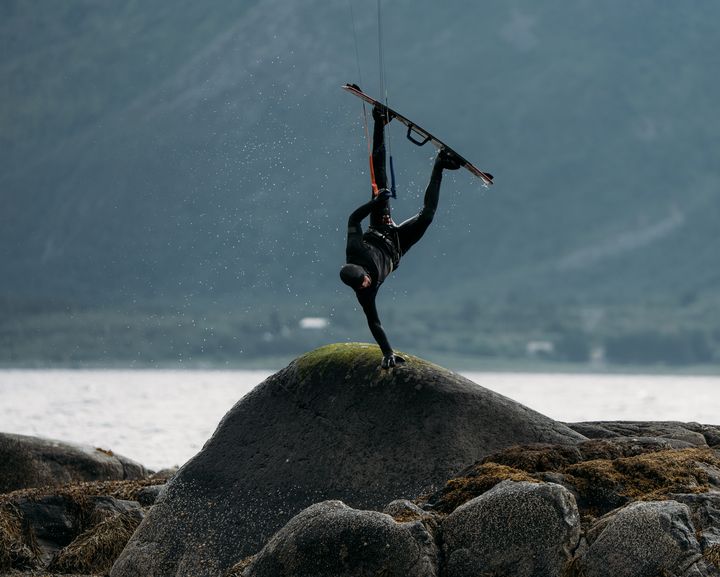 kiteboarder doing a hand plant on a rock