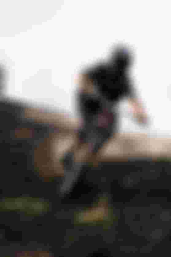 Person mountain biking downhill on a dirt trail, wearing a helmet and protective gear, with dust and debris flying, against a clear sky backdrop.