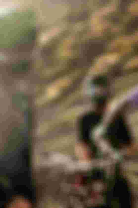 Three mountain bikers in protective gear stand with their bikes on a rugged, sunlit trail, ready for an adventure.