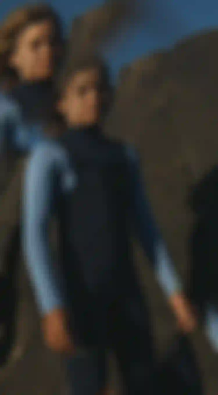 child wearing a blue wetsuit standing in front of rocks
