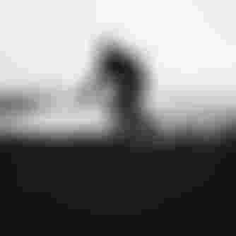 A cyclist in a helmet maneuvers a dirt trail on a mountain bike, creating a cloud of dust in a foggy, open landscape.