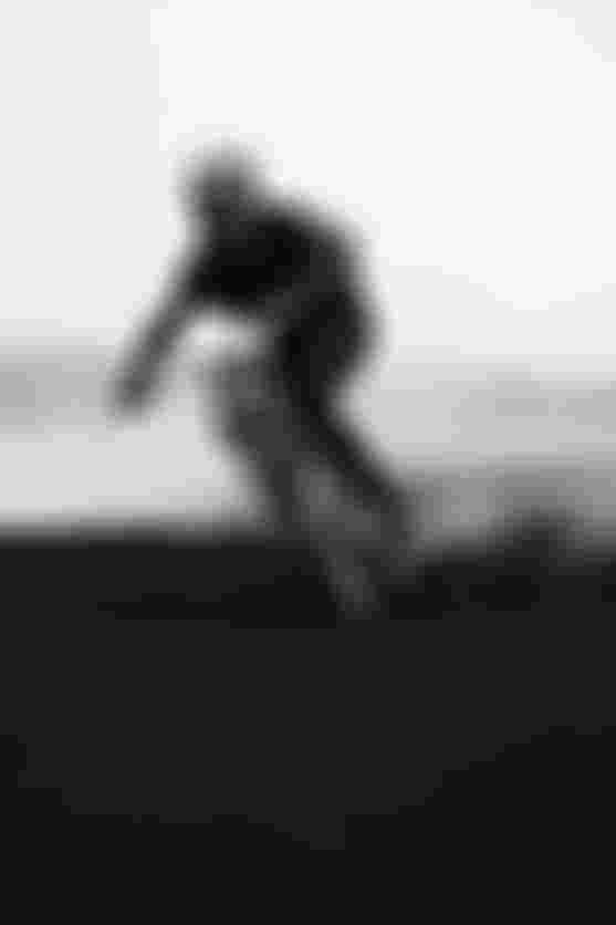 A cyclist in a helmet maneuvers a dirt trail on a mountain bike, creating a cloud of dust in a foggy, open landscape.