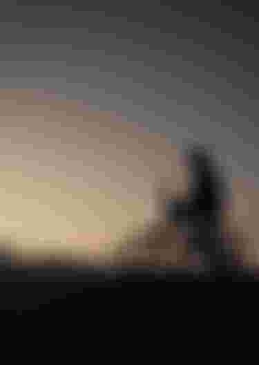 Silhouette of a person on a bicycle atop a hill at sunset, gazing at the sky.