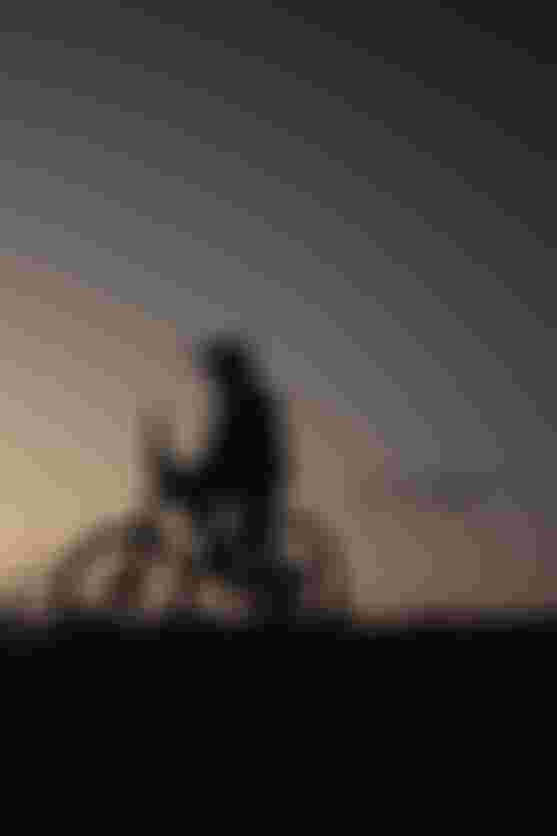 Silhouette of a person on a bicycle atop a hill at sunset, gazing at the sky.