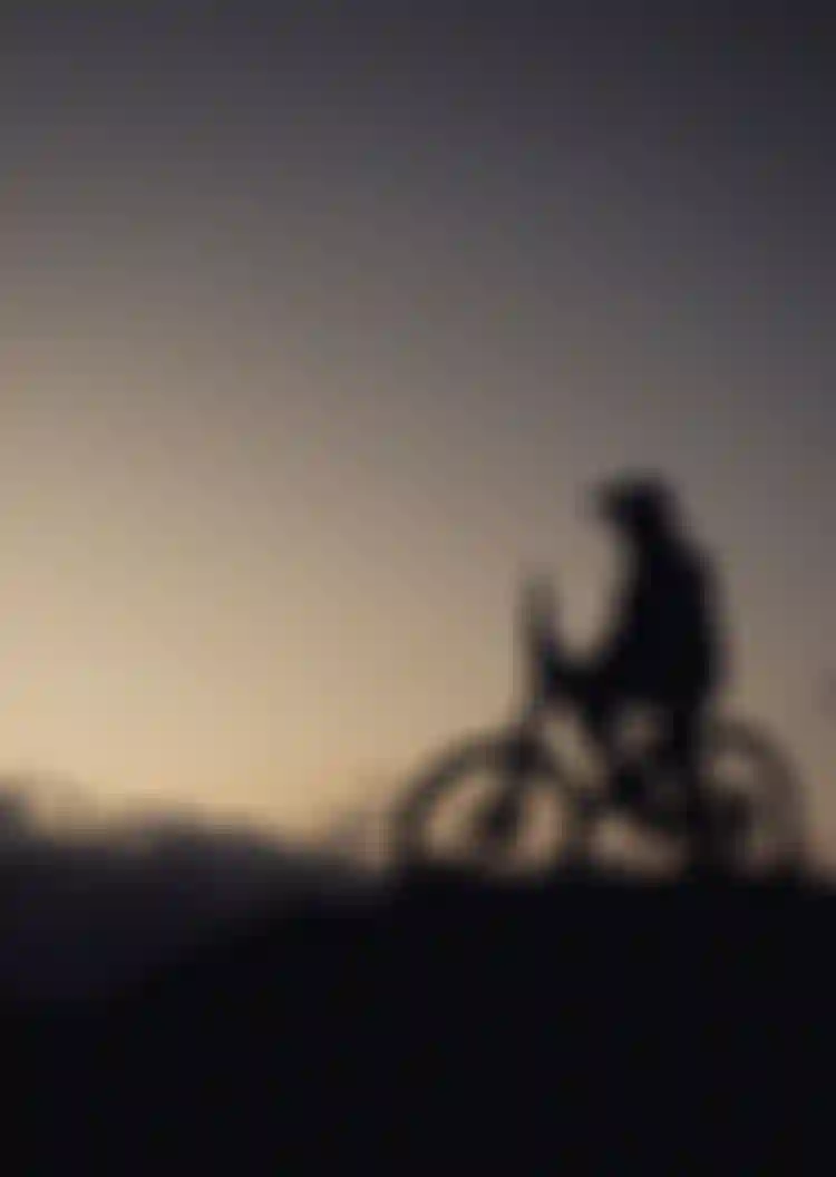 Silhouette of a person on a bicycle atop a hill at sunset, gazing at the sky.
