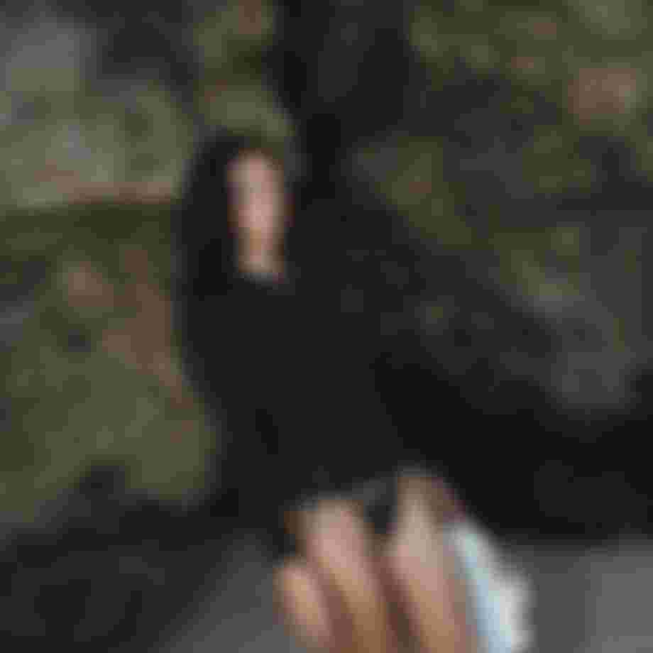 woman standing in front of rocks on a beach wearing a bikini bottom and black neoprene top