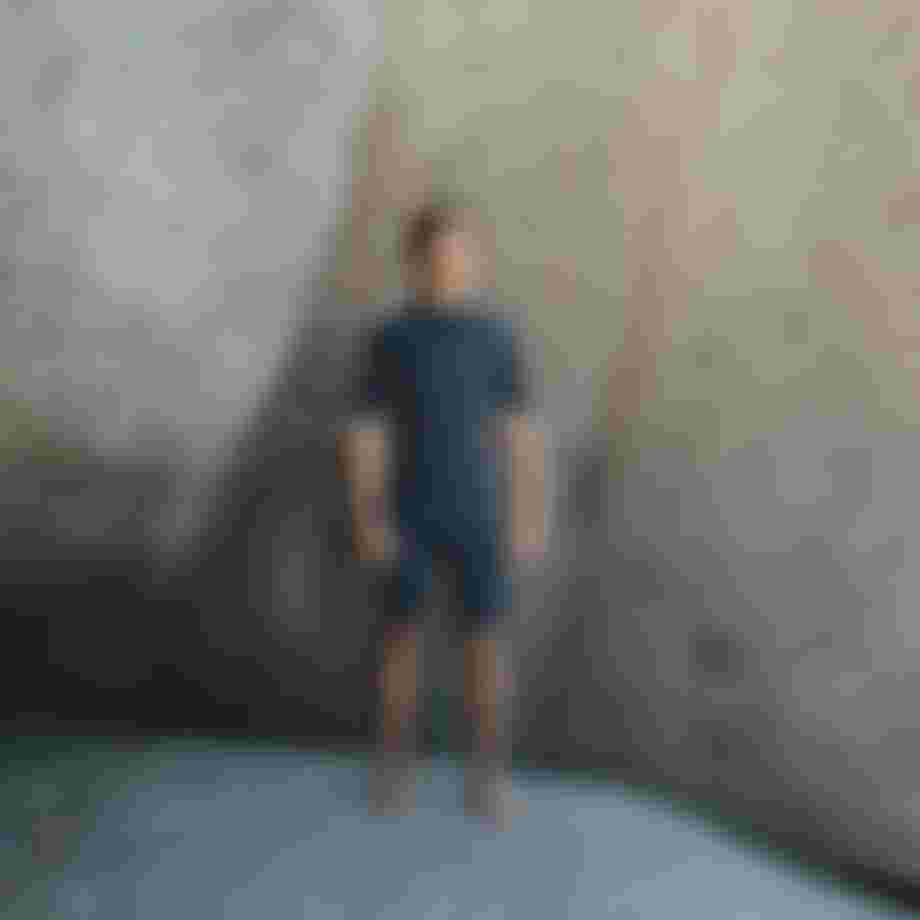 Man wearing a dark blue shorty wetsuit standing in front of big rocks