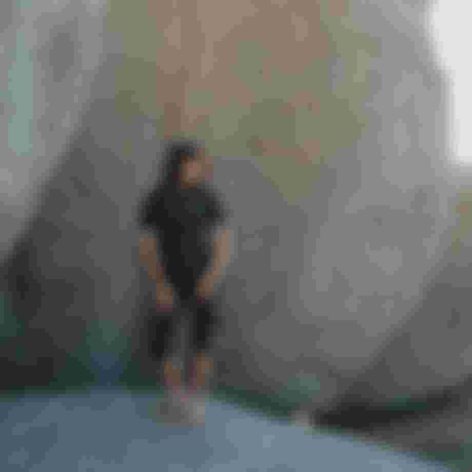Woman in black short wetsuit standing in front of big rocks
