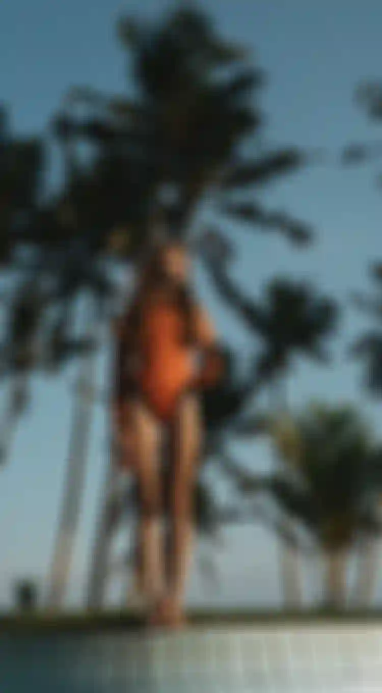 Woman in a red shorty wetsuits standing on the edge of a swimming pool