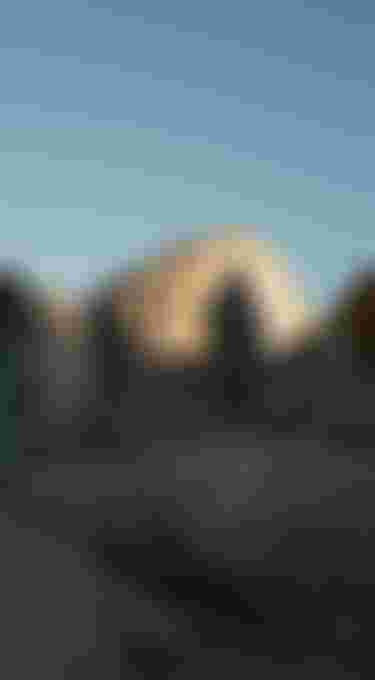 Three people wearing surf ponchos standing on big rocks with blue sky overhead