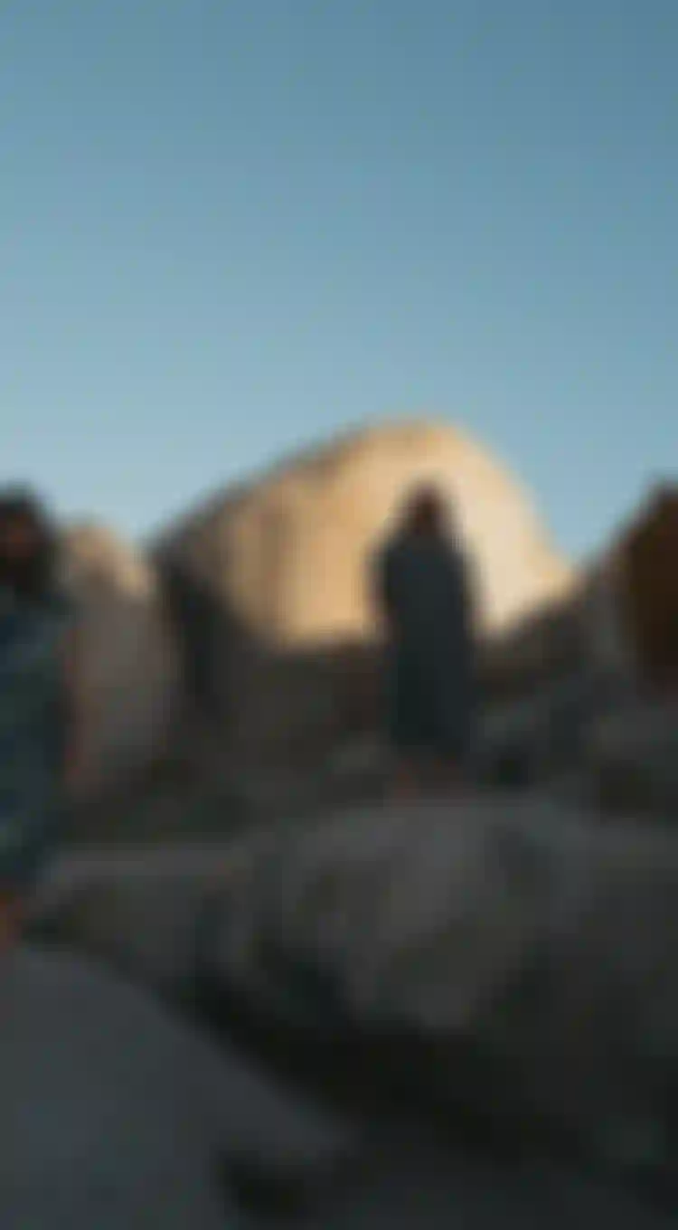Three people wearing surf ponchos standing on big rocks with blue sky overhead