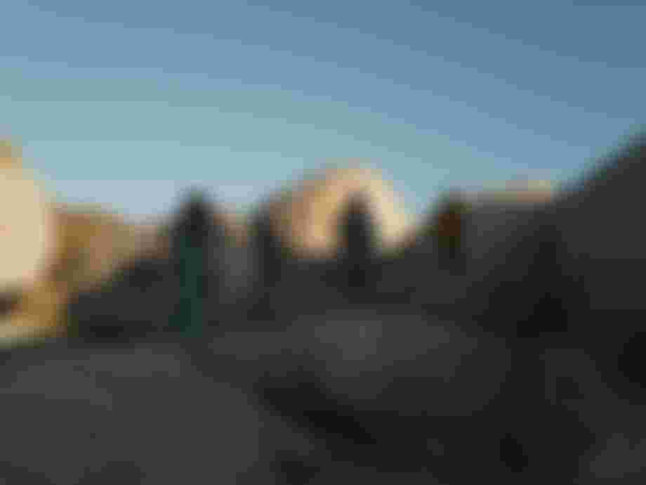 Three people wearing surf ponchos standing on big rocks with blue sky overhead