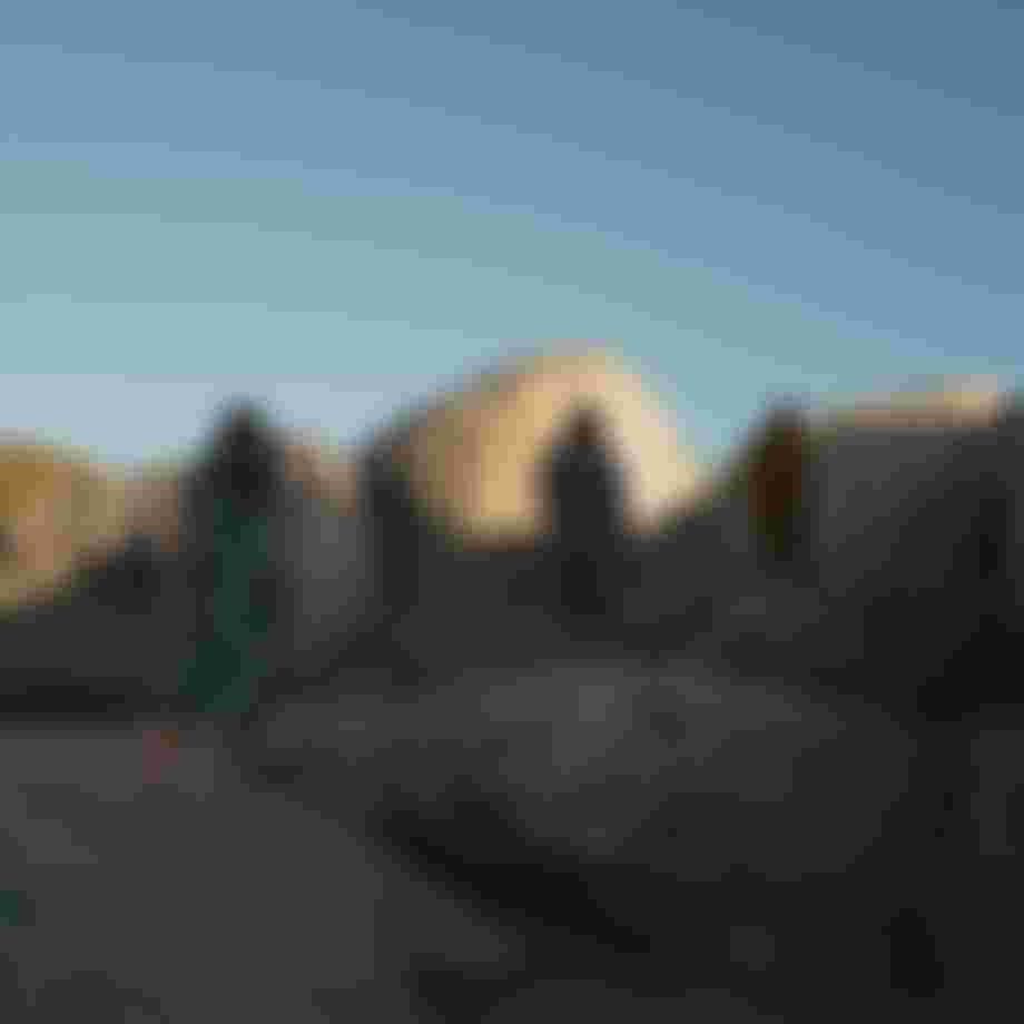 Three people wearing surf ponchos standing on big rocks with blue sky overhead