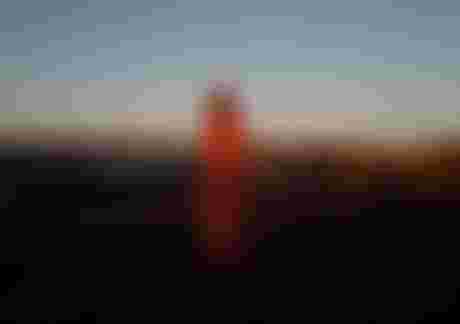 Child wearing a surf poncho with red pattern standing on a rocky beach at sunset