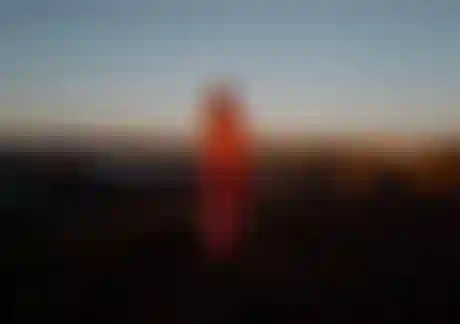 Child wearing a surf poncho with red pattern standing on a rocky beach at sunset