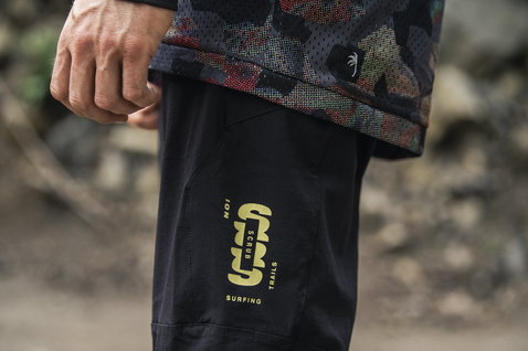 ION Scrub cycling pants in black during mountain biking on trail — thigh detail with yellow-green graphic print