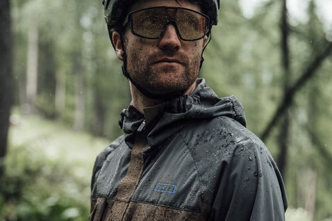 Veste cycliste ION Shelter 3L Hybrid lors d'une sortie VTT sous la pluie en forêt en gris anthracite