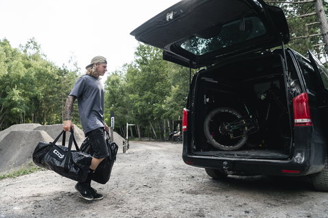 ION Universal Duffle Bag en noir porté dans un bike park en forêt