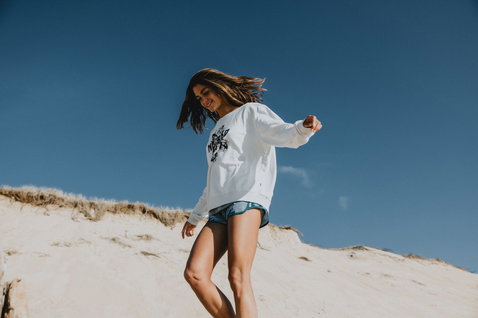 ION No Bad Days Damen-Sweater in weiß mit grafischem Print, getragen am Sandstrand unter blauem Himmel