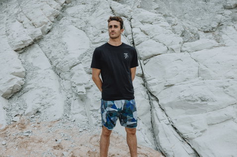 ION Avalon 18" men's boardshorts with tropical leaf print in blue and grey at rocky coast