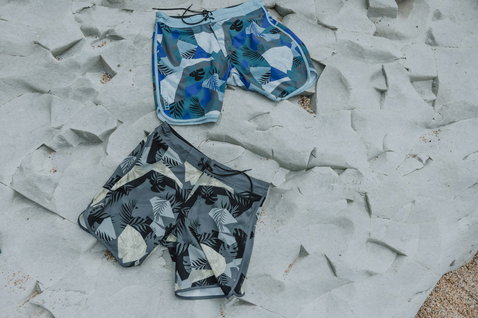 ION Avalon 18" men's boardshorts in blue-white and charcoal with tropical print, flat-lay