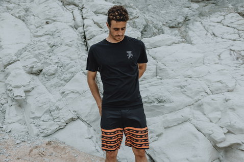 Boardshort ION Slade homme 19" en noir et corail porté sur littoral rocheux