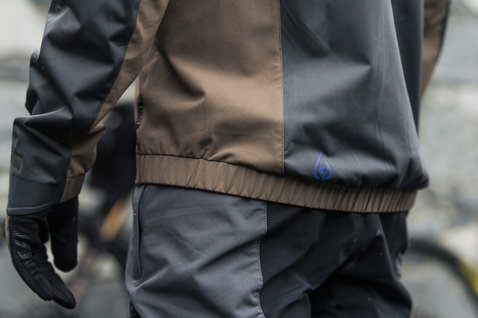 Veste de cyclisme ION Bike Shelter 3L Hybrid en noir et brun foncé lors d'une sortie VTT sous la pluie