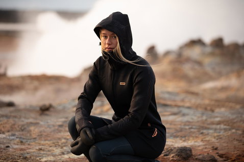 ION Neo Cosy Coat Core veste néoprène femme en noir portée sur un littoral rocheux