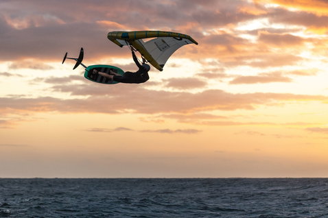 ION Water Protection Suit combinaison intégrale 3/2mm zip frontal lors de wing foiling au-dessus de l'océan au coucher du soleil